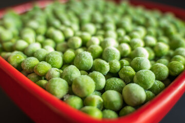 frozen frosty green peas in red ceramic bowl closeup