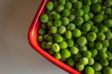 frozen frosty green peas in red ceramic bowl closeup
