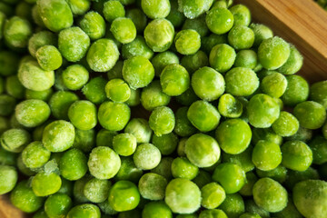 frozen frosty green peas on wooden plate closeup