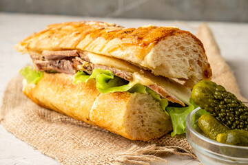 Kubanos sandwich with pork and cucumbers in a toasted baguette close-up.