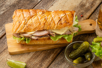 Sandwich with meat and raw materials and vegetables in a toasted bun on a wooden table.