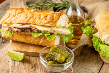 Cuban sandwich with baked meat and vegetables, toasted baguette, served on a wooden table.