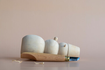 Carved wooden snowman and carving knife lies on light brown background. Few wooden shavings on the surface. Copy space for your text. Selective focus. Handmade Christmas decorations theme.