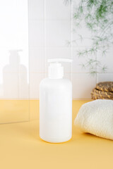 Natural Hypoallergenic Foam for bathing children. White Plastic pump bottle. children's cosmetics. Bottles on a sunny yellow background and a soft towel. Glass and green plant on the background