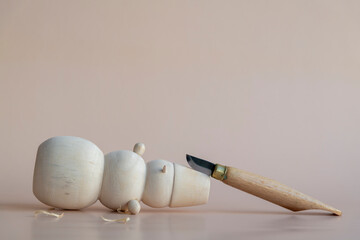 Carved wooden snowman and carving knife lies on light brown background. Few wooden shavings on the...