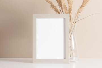 Empty wooden mockup photo frame and dried grass decoration on beige background.