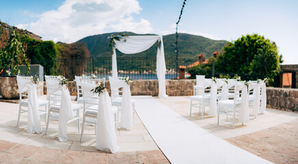 White chairs decorated with fabric stand in front of a wedding arch