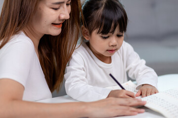 Beautiful Asian woman helping her daughter with homework at home.