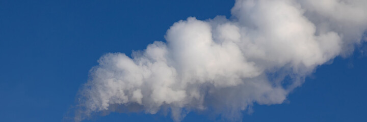 White steam or smoke is blown in the wind against the blue sky. Air pollution in city