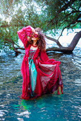 Obraz premium woman in red dress and masquerade standing in water and looking to sky