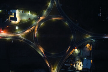 Aerial view of road roundabout intersection with fast moving heavy traffic at night. Top view of urban circular transportation crossroads. Rush hour with blurred car trail lights