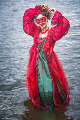 Obraz premium elegant woman in historic red dress and a masquerade standing by in water