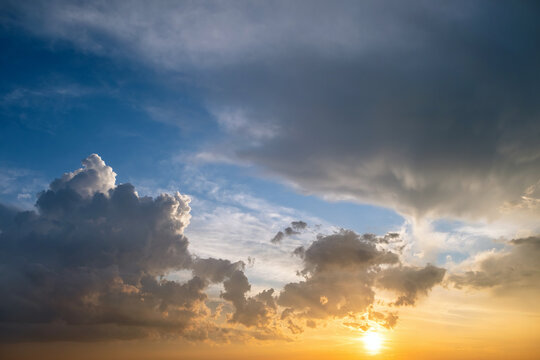 Dramatic yellow sunset landscape with puffy clouds lit by orange setting sun and blue sky. © bilanol