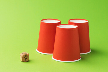 Three orange paper cups and one wooden cube with a question mark symbol, the concept of gambling and its harm