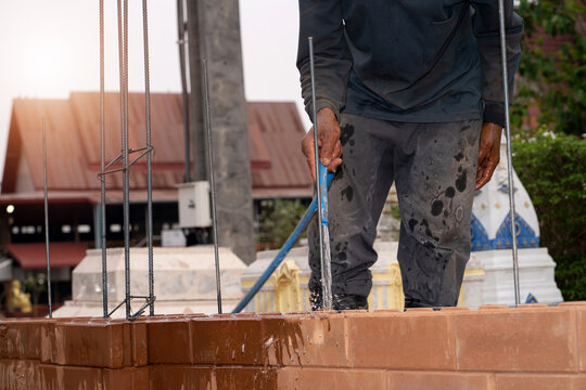 Construction worker holding a hose to water bricks, man building a brick wall, builder carrying out a construction project by himself.