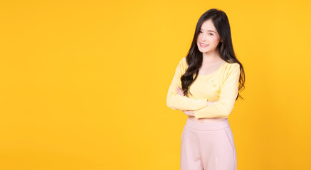 Confident charming Asian woman arms crossed standing over isolated yellow background. Cheerful student or businesswoman wear hipster style smart success while looking at camera.