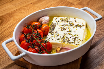 Roasted tomatoes with feta cheese and garlic served in ceramic pan on wooden table
