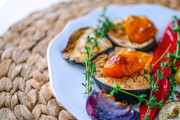 Roasted vegetables with herbs in a white plate with a fork on a background, close-up, copy space. Diet Vegetable Dinner with Baked Peppers and Eggplant
