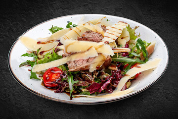 Veal and pear salad with olive-balsamic dressing. Isolated on a black background.