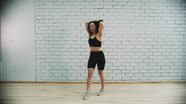 Young woman with curly hair drives weight around her head on workout