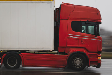 Red truck pulls a semi-trailer in the rain on the road. Close-up, motion blur