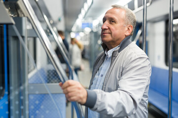 Fototapeta premium Mature man standing in subway and holding handrail