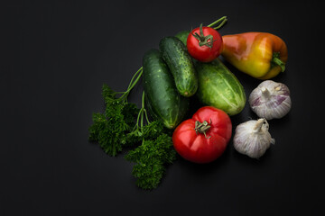 Cucumbers, tomatoes, bell peppers, garlic and herbs on a black background. Set of fresh vegetables on a black background.