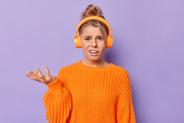 Puzzled indignant young woman wears casual knitted sweater raises palm feels clueless cannot hear...
