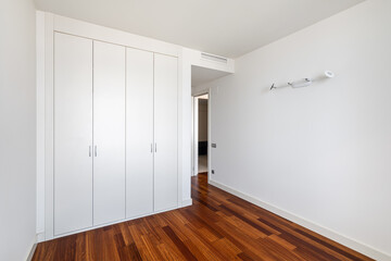 Interior of empty apartment, white room with built-in wardrobe and parquet floor