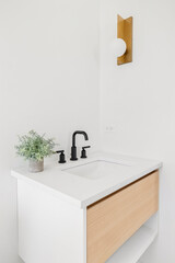 A modern bathroom with a wood vanity cabinet, black faucet and white marble countertop, and a gold...