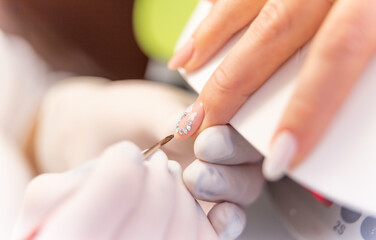 manicurist glues colored stones and paints on the manicure of a client.