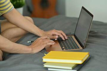 Cropped image of a university student doing homework with a white blank screen computer laptop on the bed.