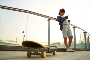 teenage asian skateboarder boy looking at cellphone