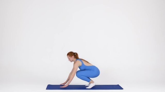 Sporty young female making burpee exercise on fitness mat in studio