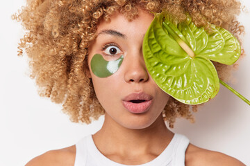 Spa portrait. Surprised woman with curly hair has bugged eyes hides face with green calla applies...