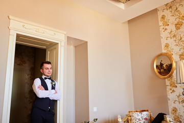 Stylish groom stands near a large window. Wedding portrait of a young man in a room, studio. The morning of the groom. Wedding portrait of a stylish male.