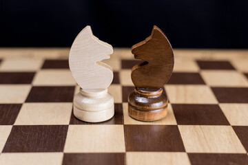 Two chess knights are facing each other on the chessboard. The concept of rivalry, duel, battle, struggle, two opposing sides, enemies, opposition, enmity.