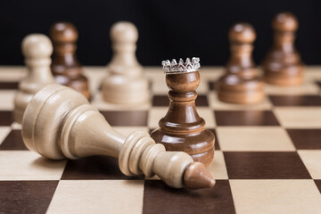 A black chess pawn with a crown on the chessboard, a defeated white chess king lies next to it. The...