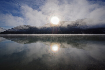 Alpiner Stausee Sylvensteinspeicher im morgendlichen Nebel und Kondensstreifen an einem kalten Tag...