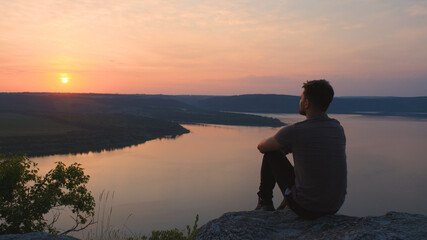 The young man sitting on rocky mountain above the beautiful river