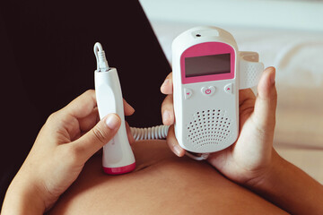 The close up pregnant woman using pocket fetal doppler to monitor baby heart beat.