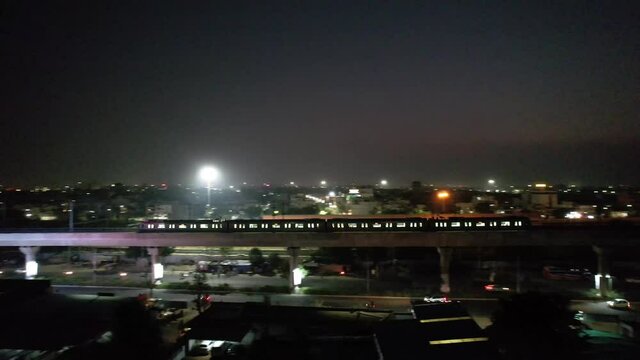 long distance right to left pan showing metro train on elevated bridge moving across the screen showing the dark cityscape of jaipur showing traffic and the dusk colors and public transport