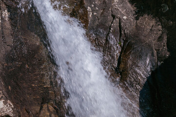 kleiner Wasserfall in bergiger und waldiger Landschaft an einem sonnigen Herbsttag