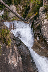 kleiner Wasserfall in bergiger und waldiger Landschaft an einem sonnigen Herbsttag
