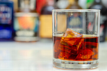 Old fashioned glass with scotch whisky and ice cubes on the bar