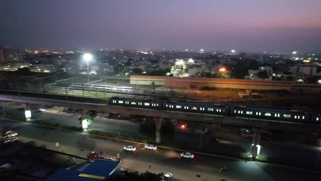 panning dusk twilight night shot of metro moving on bridge and cars moving below on the road showing the cityscape of jaipur city in the distance showing the rapid development of infrastructure