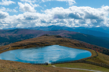 K&uuml;nstlich angelegter Teich in den Bergen von &Ouml;sterreich. Blick auf die berge und den wolkigen Himmel