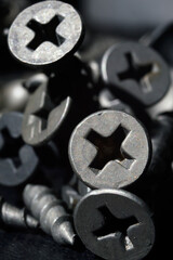 black hardened self-tapping screws lies on a dark background. close-up.