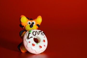 A toy tiger made of plasticine with a cake in his hand on a red background.