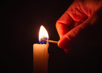 Lit wooden matchstick lighting a candle in darkness. Blackout city or power outage, symbolic image